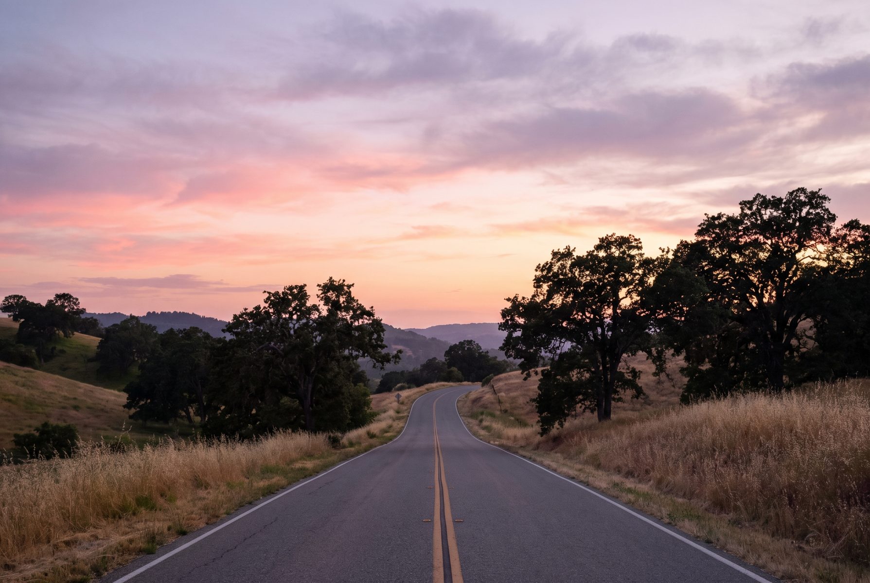 A long winding country road at dusk with soft pink sky, no people, calm and open